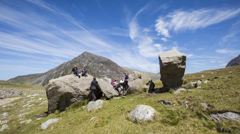 Ymwelwyr yn ymlacio ar glogfeini a elwir yn Glogfeini Darwin yng Nghwm Idwal gyda Phen yr Ole Wen yn y cefndir yn y Carneddau a’r Glyderau, Gwynedd. Cymru.